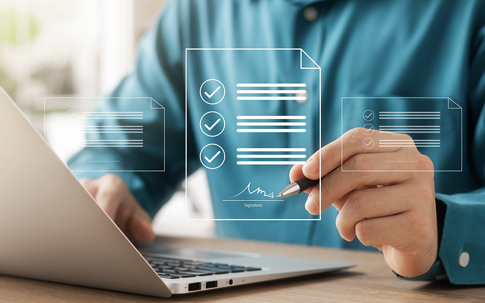 person with laptop on desk signing a digital paper in front of them. Depicting an automated signature verification process